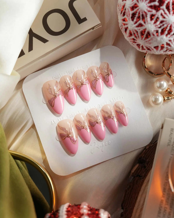 Pink French press-on nails with gold bow details and glossy finish