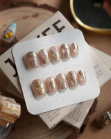 Plume press-on nails in extra short coffin shape — Elegant Nude, Brushed Gold Foil Feathers & Fluid Textures.