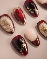Gilded Merlot press-on nails with deep red cat-eye, nude French tips and gold rose reliefs