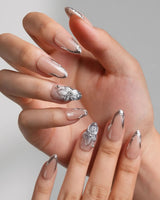 Silver Shore medium almond nails with nude base, sculpted silver French tips, and 3D metallic flower