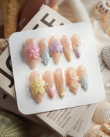 Sunbathing medium stiletto nails with iridescent nude pastels, florals, and shells