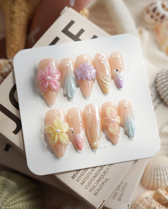Sunbathing medium stiletto nails with iridescent nude pastels, florals, and shells