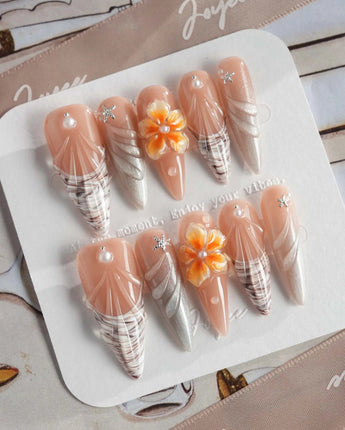 Sunset Shore long stiletto nails with sunset coral, 3D blossoms, and shell accents