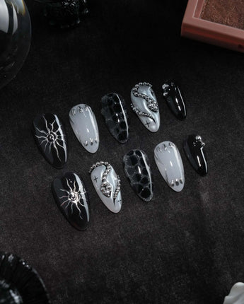 Talisman press on nails with a raised silver spiral sun on black, chrome white, glitter web print and a pearl nail crossed with silver beads - image 3