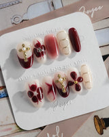 Tip Burgundy Nails in medium oval shape with burgundy French tips and gold floral accents