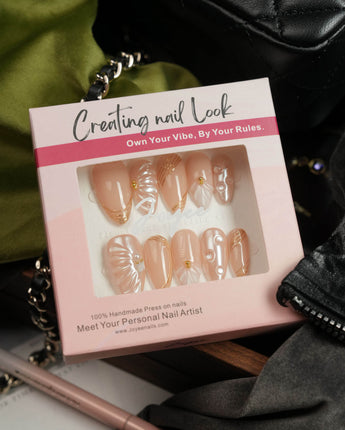 Venus medium almond nails with pearly nude base, shells, and gold details